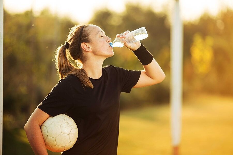 Frau hält Fußball in der Hand und trinkt aus einer Wasserflasche