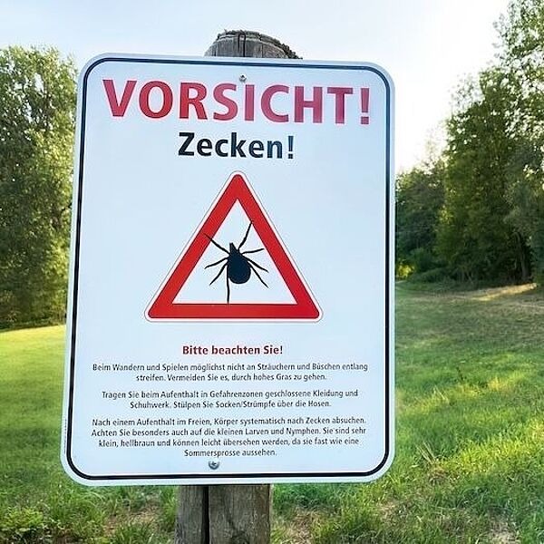 Schild auf einer Wiese mit Aufschrift "Vorsicht! Zecken!"